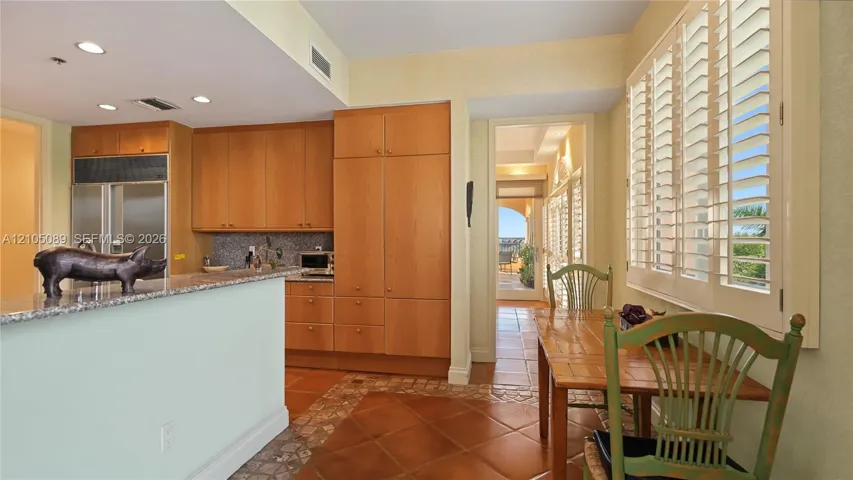 Kitchen featuring wood cabinetry, stone countertops, tiled flooring, recessed lighting, and plantation shutters