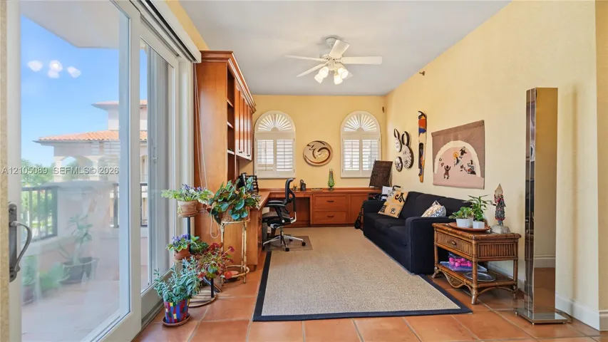 Custom wood-finish built-in cabinetry, arched windows with plantation shutters, large-format terracotta tile flooring, sliding glass door, and a ceiling fan with integrated lighting