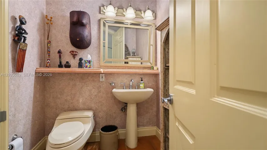 Pedestal sink with chrome faucet, stone-surfaced floating shelf, framed wall mirror, three-light fixture with glass shades, and neutral wall finish