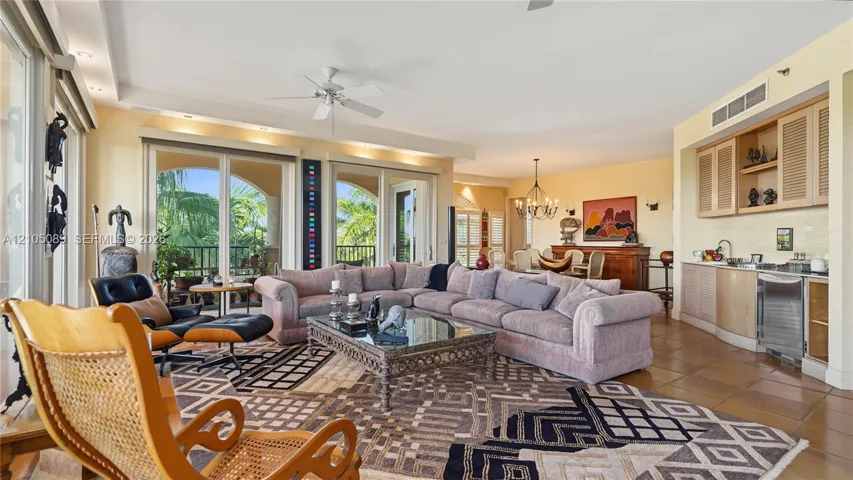 Open-concept living space featuring ceramic tile flooring, built-in wet bar with light wood cabinetry, multi-panel sliding glass doors, and recessed ceiling lighting