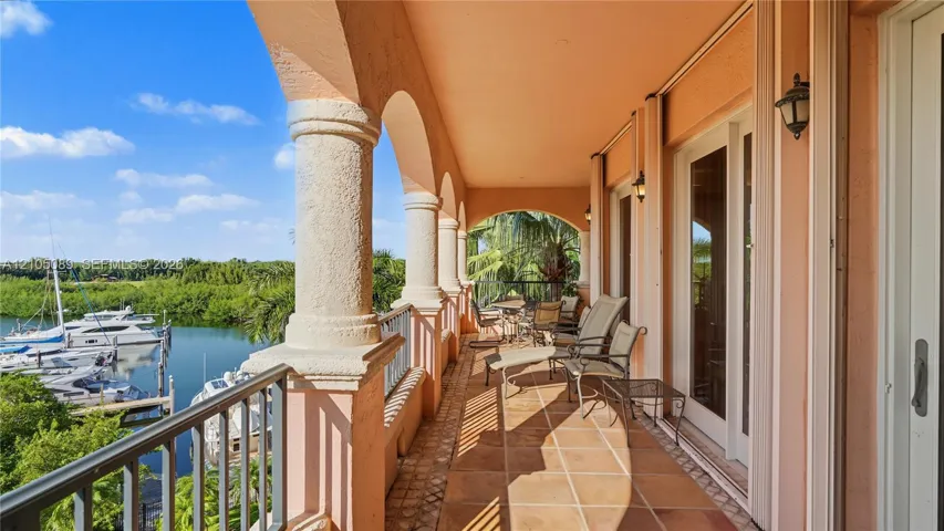 Covered balcony featuring arched architectural columns, tile flooring, metal railings, and exterior wall-mounted lighting