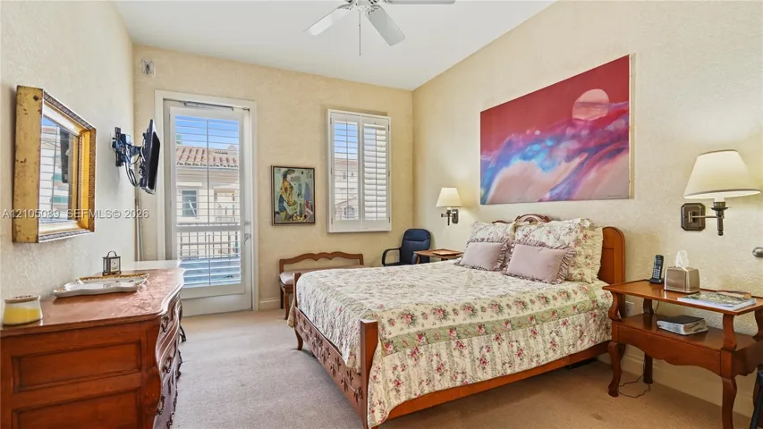 High-ceilinged room featuring a ceiling fan, dual wall-mounted light fixtures, plantation shutters, and a glass-paneled door