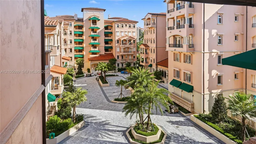 Multi-story stucco exterior featuring tile roofing, wrought iron balcony railings, arched architectural details, and a stone-paved courtyard with mature palm landscaping