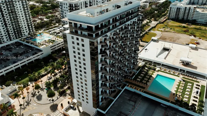 Multi-story building featuring numerous private balconies, a rooftop deck, and an adjacent outdoor swimming pool with surrounding lounge areas