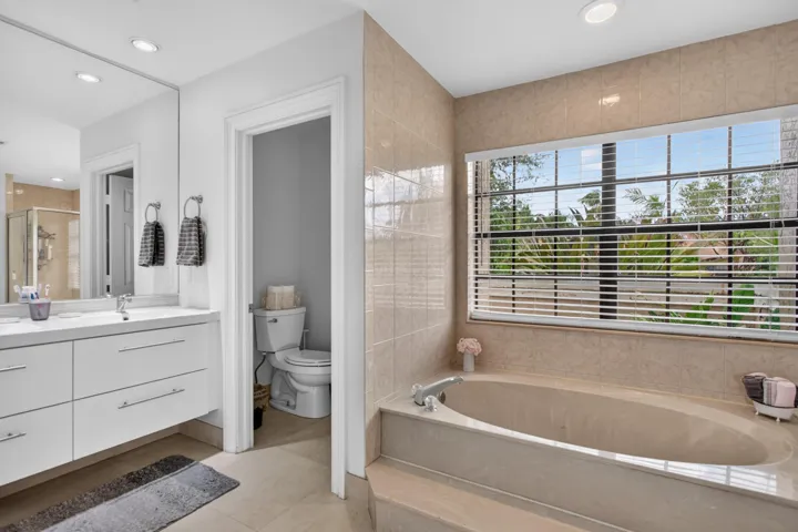Recessed lighting, large vanity mirror, built-in bathtub, tiled surround, and large window
