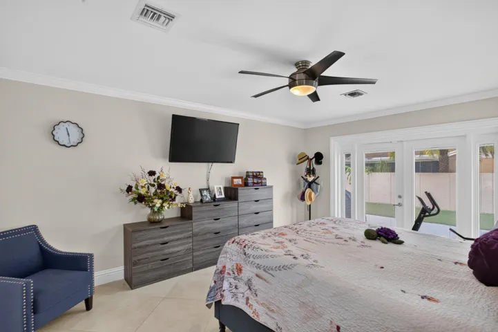 Crown molding, ceiling fan with integrated lighting, wall-mounted television, and direct access to an outdoor area through glass panel doors