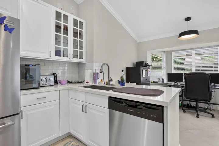 White shaker cabinetry, subway tile backsplash, stainless steel dishwasher, undermount sink with a gooseneck faucet, and a vaulted ceiling