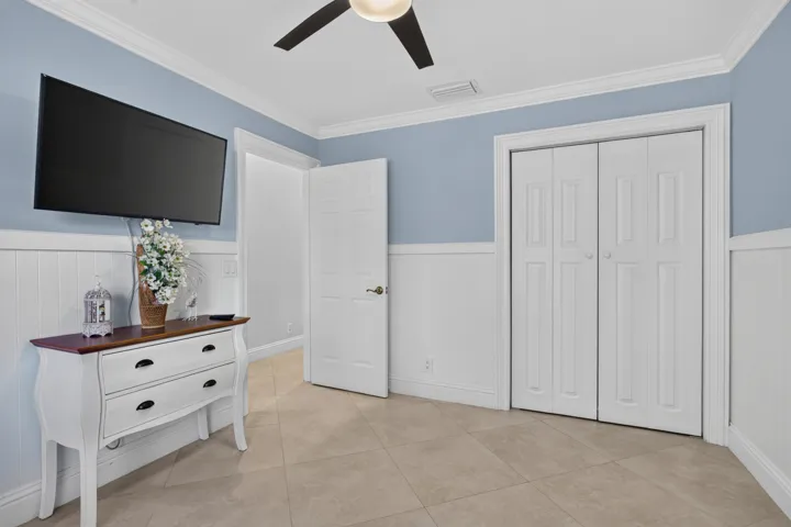 Ceiling fan, wall-mounted television, white paneling, bi-fold closet doors, tile flooring