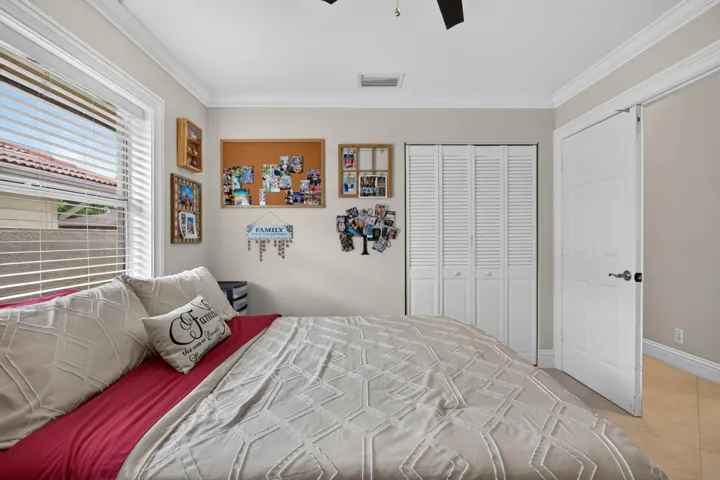 White bi-fold louvered closet doors, crown molding, a ceiling fan, and tile flooring