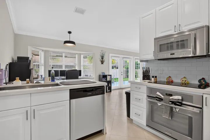 White shaker cabinetry, stainless steel appliances, bay windows, tile flooring, and a subway tile backsplash
