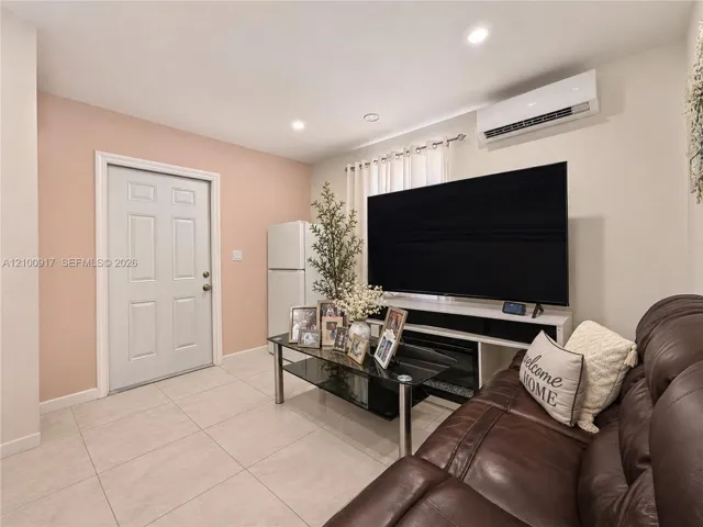 Recessed ceiling lighting, wall-mounted air conditioning unit, white paneled door, and light-toned tile flooring