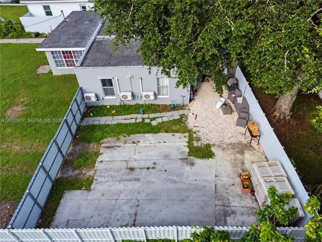 Fenced outdoor space featuring a paved area, gravel section, and mature trees