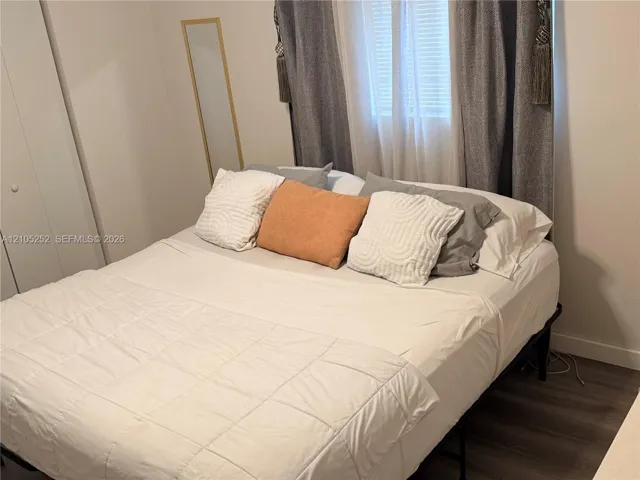 Wood-finish flooring with a window featuring blinds and drapes