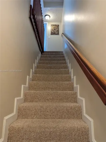 Staircase featuring wall-to-wall carpeting, wood-finish handrail, and open-slat wood balustrade
