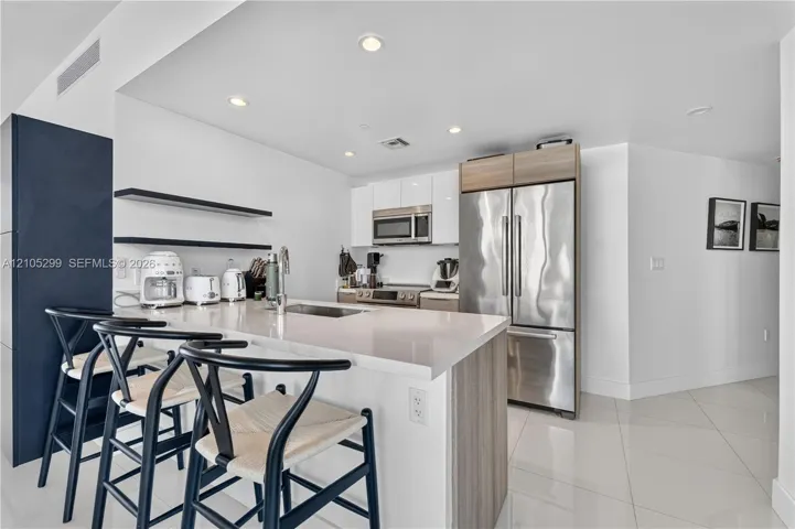 Contemporary kitchen featuring stainless steel appliances, a center island with bar seating, white stone countertops, and recessed lighting