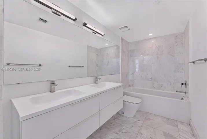 Dual-sink vanity with under-mount sinks, a wide mirror, a tub with a tiled surround, and tiled flooring