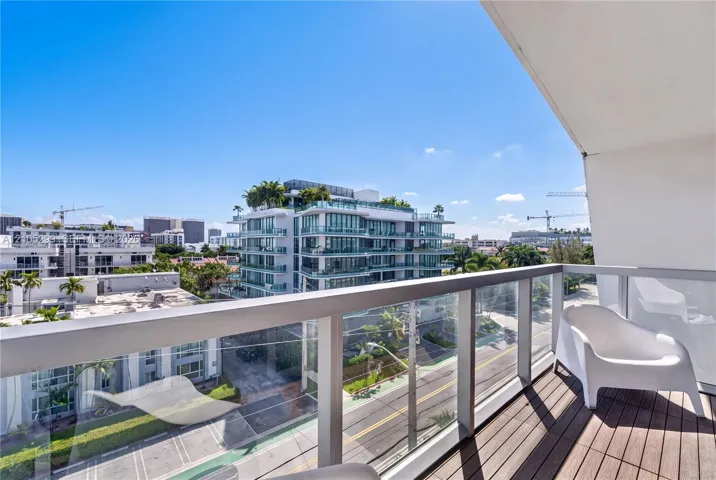 Balcony featuring wood-finish flooring, glass panel railing, and a vibrant urban backdrop