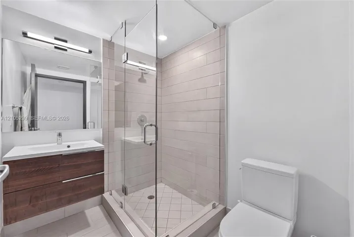 Floating wood-finish vanity with an integrated sink, large vanity mirror, glass-enclosed shower with tile surround, and an elongated toilet