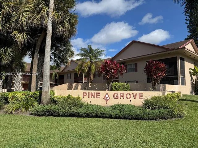 Prominent property signage, mature palm trees, established landscaping, screened outdoor living spaces, and a neutral-toned building exterior