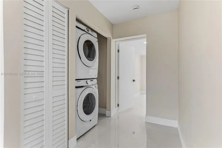 Laundry closet featuring a stacked washer and dryer, white louvered bifold doors, and a tiled floor
