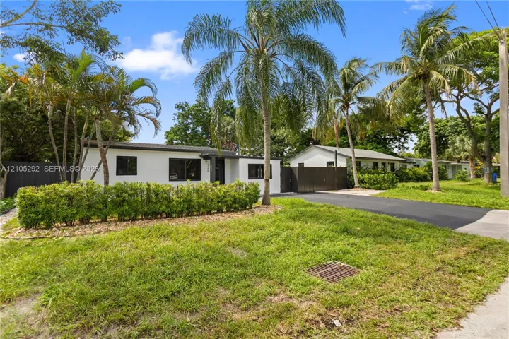 White exterior with dark-framed windows, surrounded by mature palm trees and lush landscaping