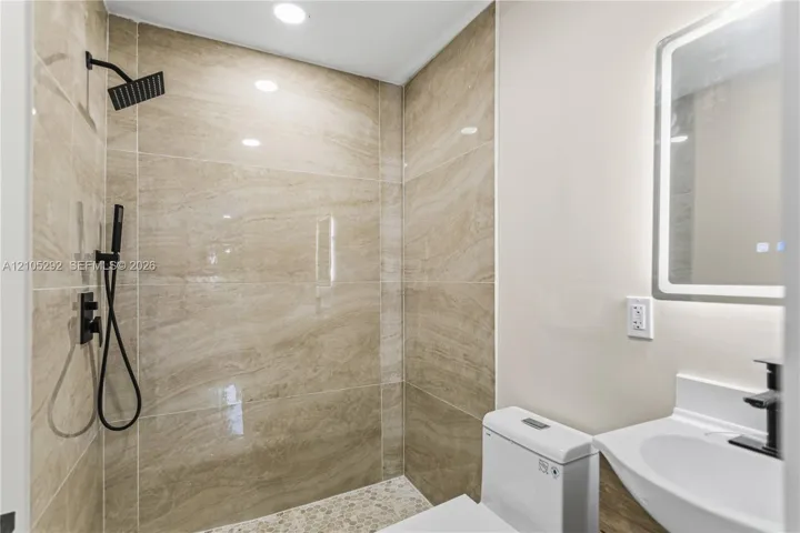 Walk-in shower with natural stone-look tile, pebble floor, and matte black fixtures
