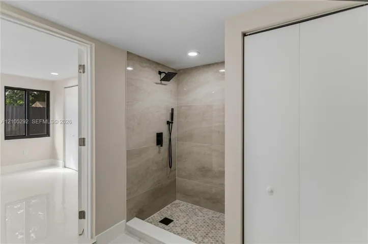 Walk-in shower with tiled walls and floor, featuring matte black fixtures and recessed lighting