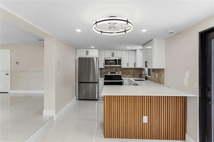 Kitchen with white cabinetry, stainless steel appliances, a tile backsplash, and a breakfast bar with a wood-slat base