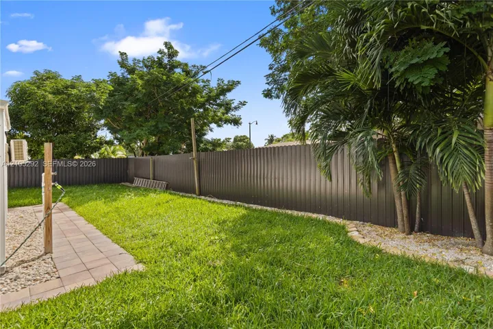 Lush green lawn with a privacy fence, mature trees, and a paver walkway