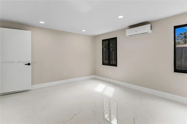 Recessed ceiling lighting, white tile flooring, mini-split air conditioning unit, white interior door with black hardware, and black-framed windows