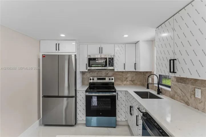 Stainless steel refrigerator, integrated microwave, built-in range, single basin sink with a matte black faucet, and white countertops
