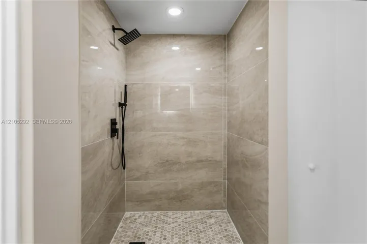 Walk-in shower with large-format wall tiles, hexagonal floor tiles, and matte black shower fixtures