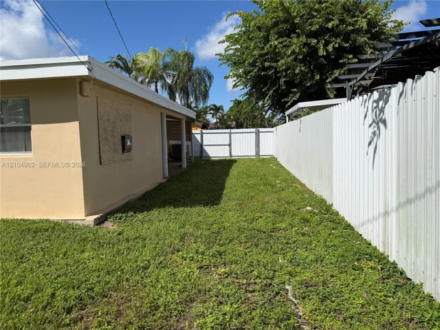 Enclosed grassy area featuring a white corrugated fence and a metal gate