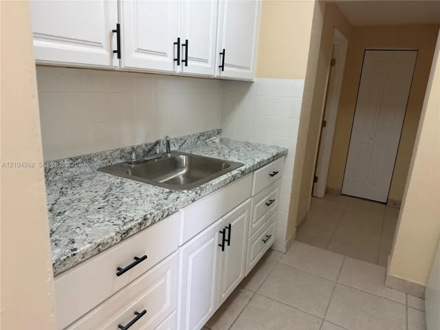 White cabinetry with black bar pulls, a stainless steel sink, a speckled countertop, and a tiled backsplash