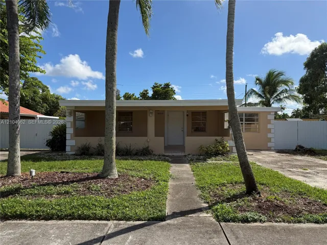 Single-story residence featuring a paved walkway, mature palm trees, and a white privacy fence