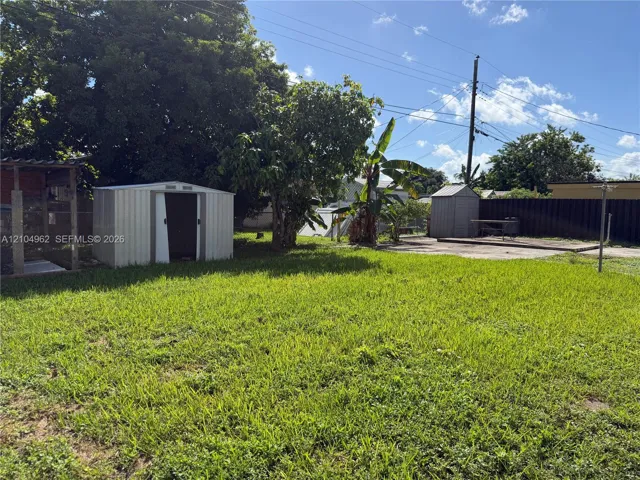 Expansive grassy yard area featuring mature trees, a metal storage shed, and a concrete patio