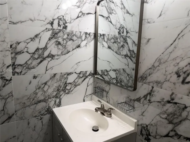 Full-height wall tiling with a marble-effect finish, a vanity with an integrated sink, and a framed mirror