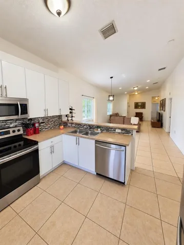Kitchen featuring a stainless steel appliance suite, white cabinetry with brushed nickel hardware, a mosaic tile backsplash, and light-toned tile flooring