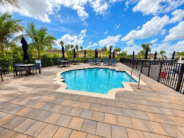 Freeform swimming pool with a black wrought iron fence, natural stone coping, and paver decking
