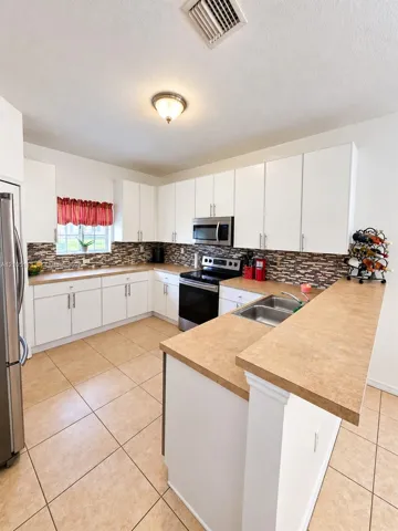 Kitchen featuring white cabinetry, tile flooring, stainless steel appliances, a double basin sink, and a multi-toned backsplash