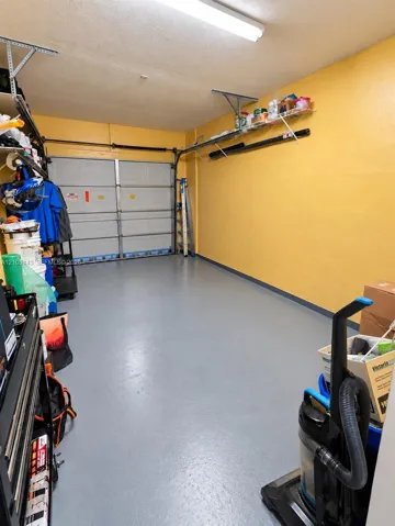 Attached garage featuring a light gray finished floor, overhead lighting, and built-in shelving