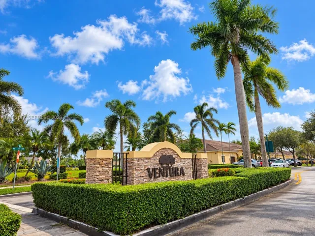 Gated community entrance featuring stone-finish pillars, wrought iron accents, and manicured hedges