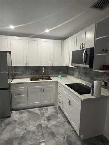 Kitchen featuring white shaker cabinetry, light-toned countertops, a built-in microwave, and a flush-mounted cooktop