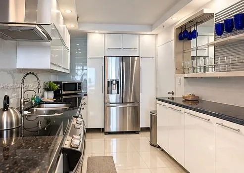 Modern kitchen with white cabinetry, stainless steel appliances, dark stone countertops, and tile flooring
