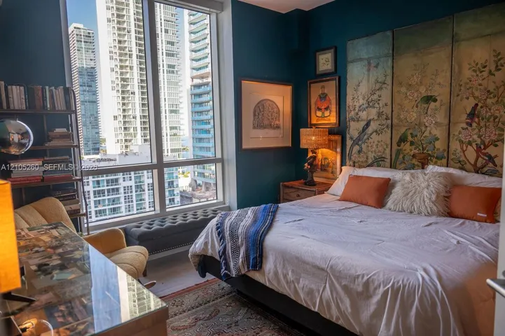 Floor-to-ceiling window offering cityscape, dark accent wall, wood-finish flooring, built-in shelving, and a decorative headboard panel