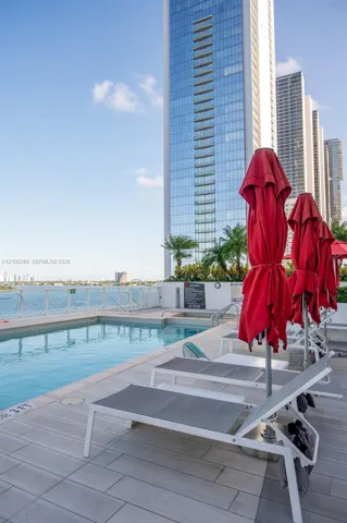 Outdoor pool area with a water body backdrop, multiple lounge chairs, and a contemporary high-rise building