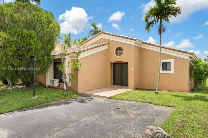 Stucco exterior with a tile roof, featuring a circular window and a paved entry