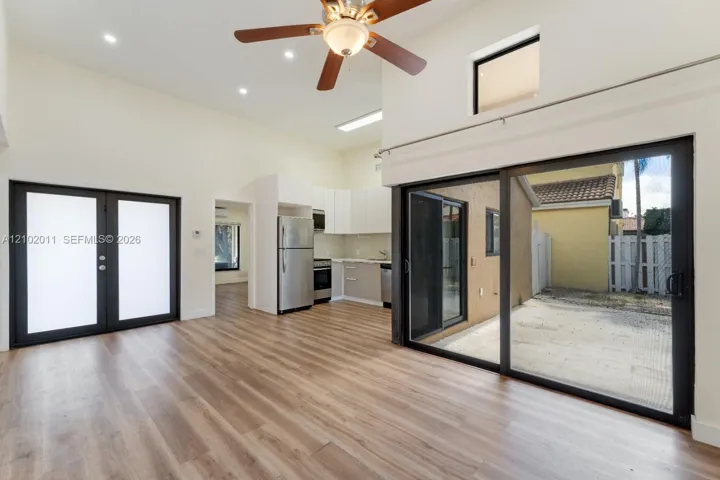 Vaulted ceilings with recessed lighting, wood-finish flooring, sliding glass doors to outdoor space, stainless steel appliances, and white cabinetry with a light-colored countertop