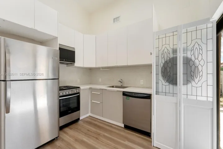 Kitchen featuring stainless steel appliances, white upper cabinetry, light gray lower cabinetry, light-toned countertops, and wood-finish flooring