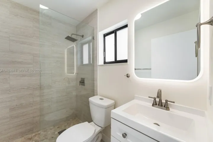 Glass-enclosed shower with rain showerhead, pebble-tiled shower floor, and tiled walls